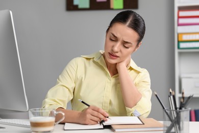 Young woman suffering from neck pain while working at table in office