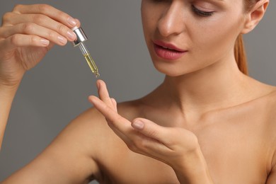 Photo of Beautiful young woman applying cosmetic serum onto her finger on grey background, closeup