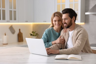 Photo of Happy couple with laptop at white table in kitchen