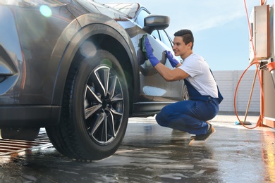 Photo of Male worker cleaning automobile door with rag at car wash