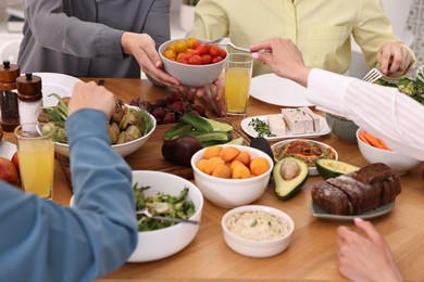 Friends eating vegetarian food at wooden table indoors, closeup