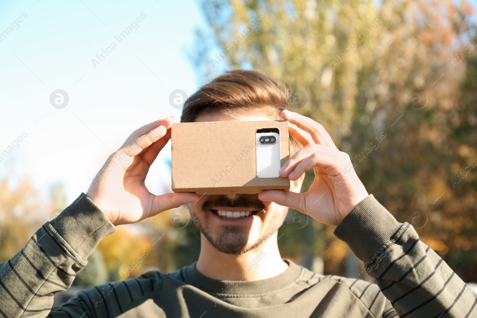 Photo of Young man using cardboard virtual reality headset outdoors