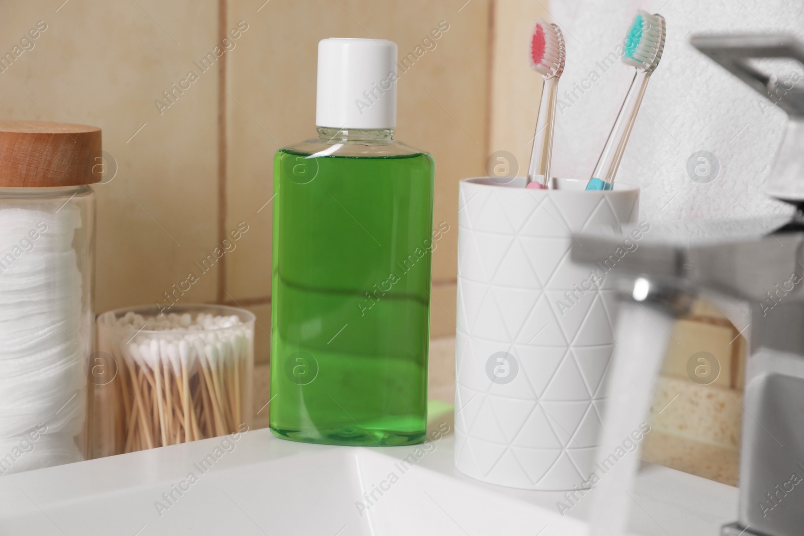 Photo of Fresh mouthwash in bottle and holder with toothbrushes on sink in bathroom