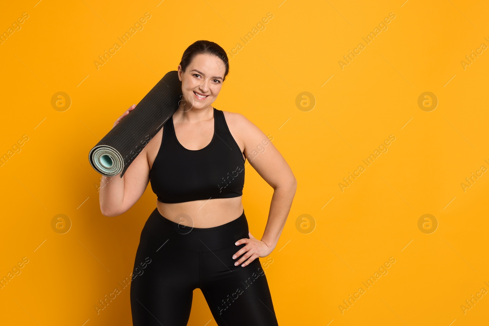 Photo of Happy overweight woman with yoga mat on orange background, space for text