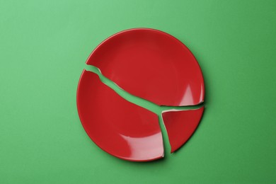 Photo of Pieces of broken ceramic plate on green background, flat lay