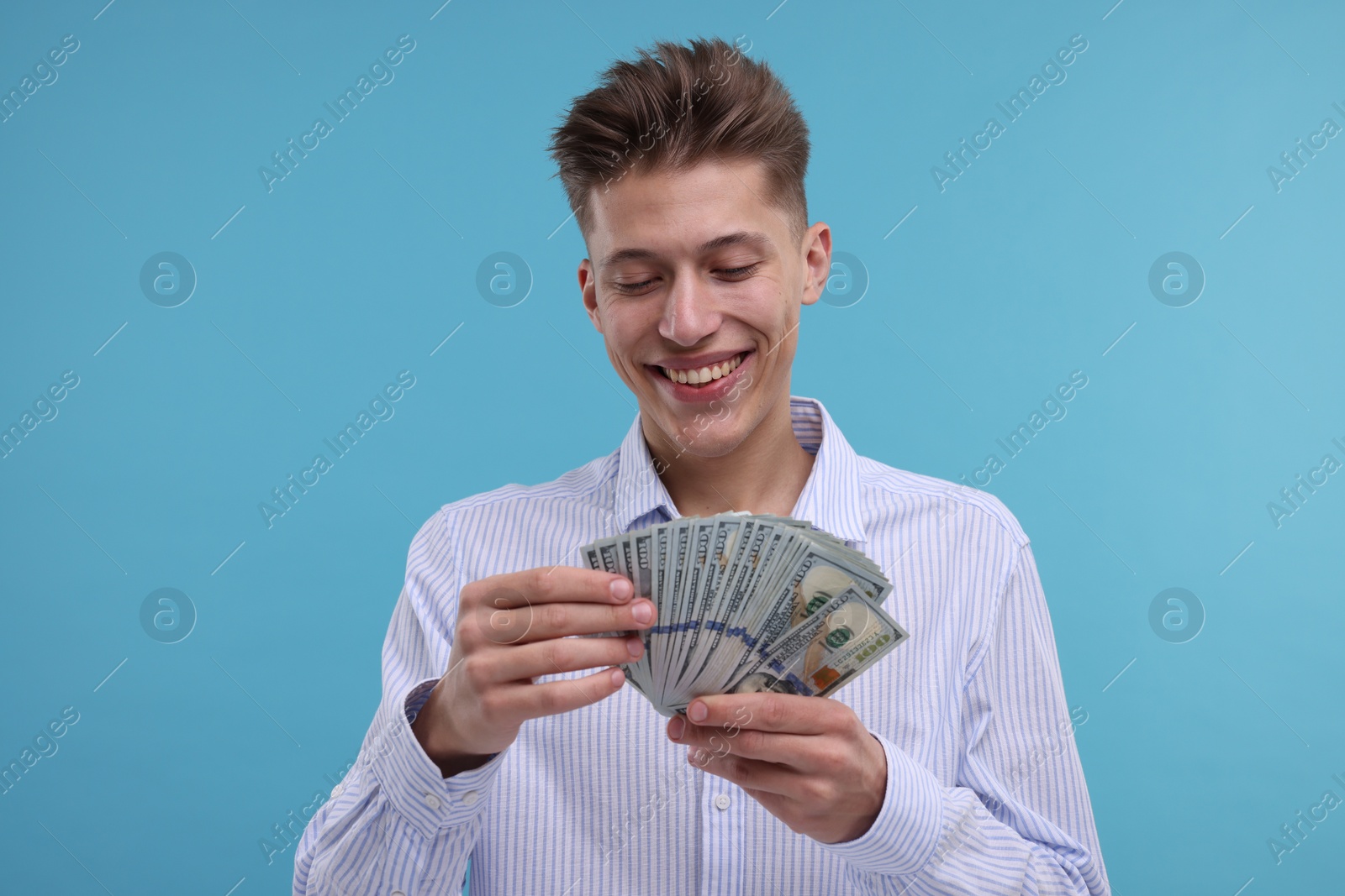 Photo of Happy man counting dollar banknotes on light blue background