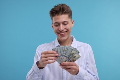 Happy man counting dollar banknotes on light blue background