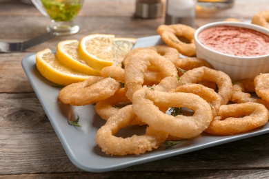 Fried onion rings served with sauce and lemon slices on plate, closeup