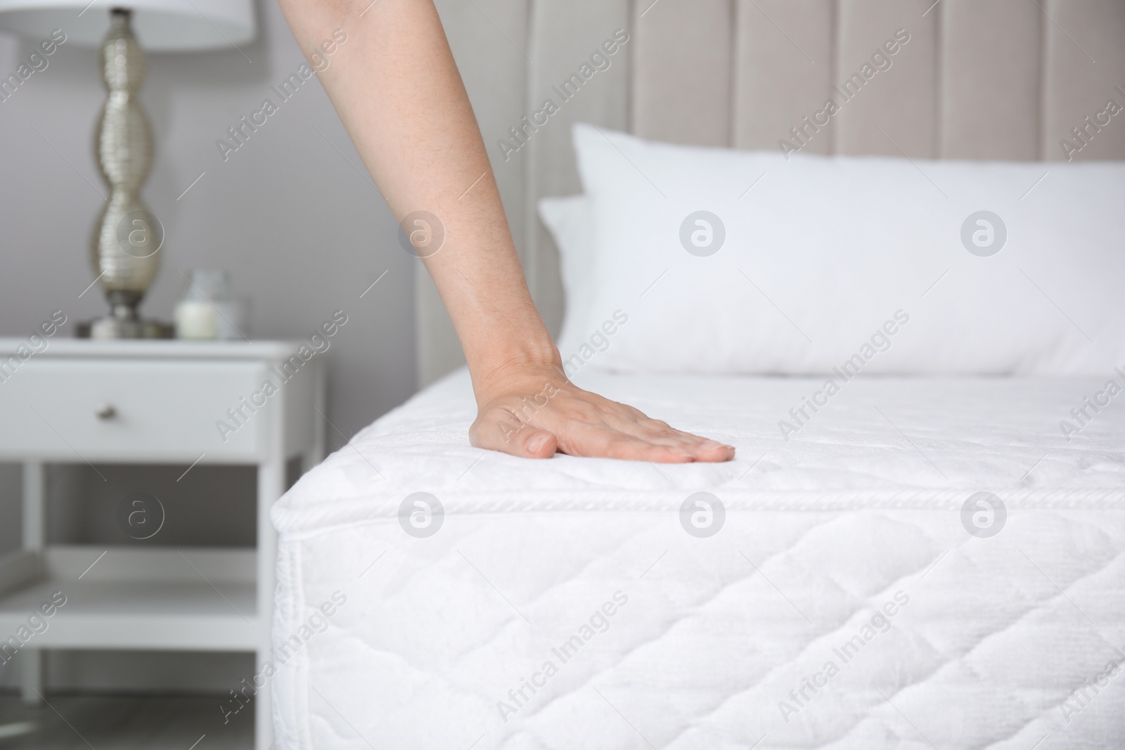 Photo of Woman touching soft white mattress on bed indoors, closeup