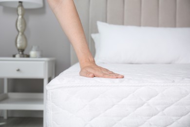 Woman touching soft white mattress on bed indoors, closeup