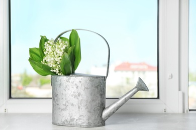 Watering can with lily of the valley bouquet on windowsill, space for text