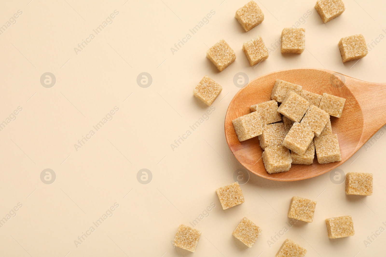 Photo of Brown sugar cubes and wooden spoon on beige background, flat lay. Space for text