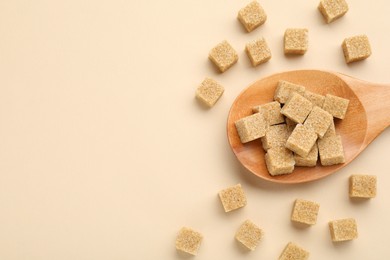 Photo of Brown sugar cubes and wooden spoon on beige background, flat lay. Space for text