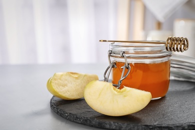 Slate plate with jar of honey, sliced apples and dipper on table