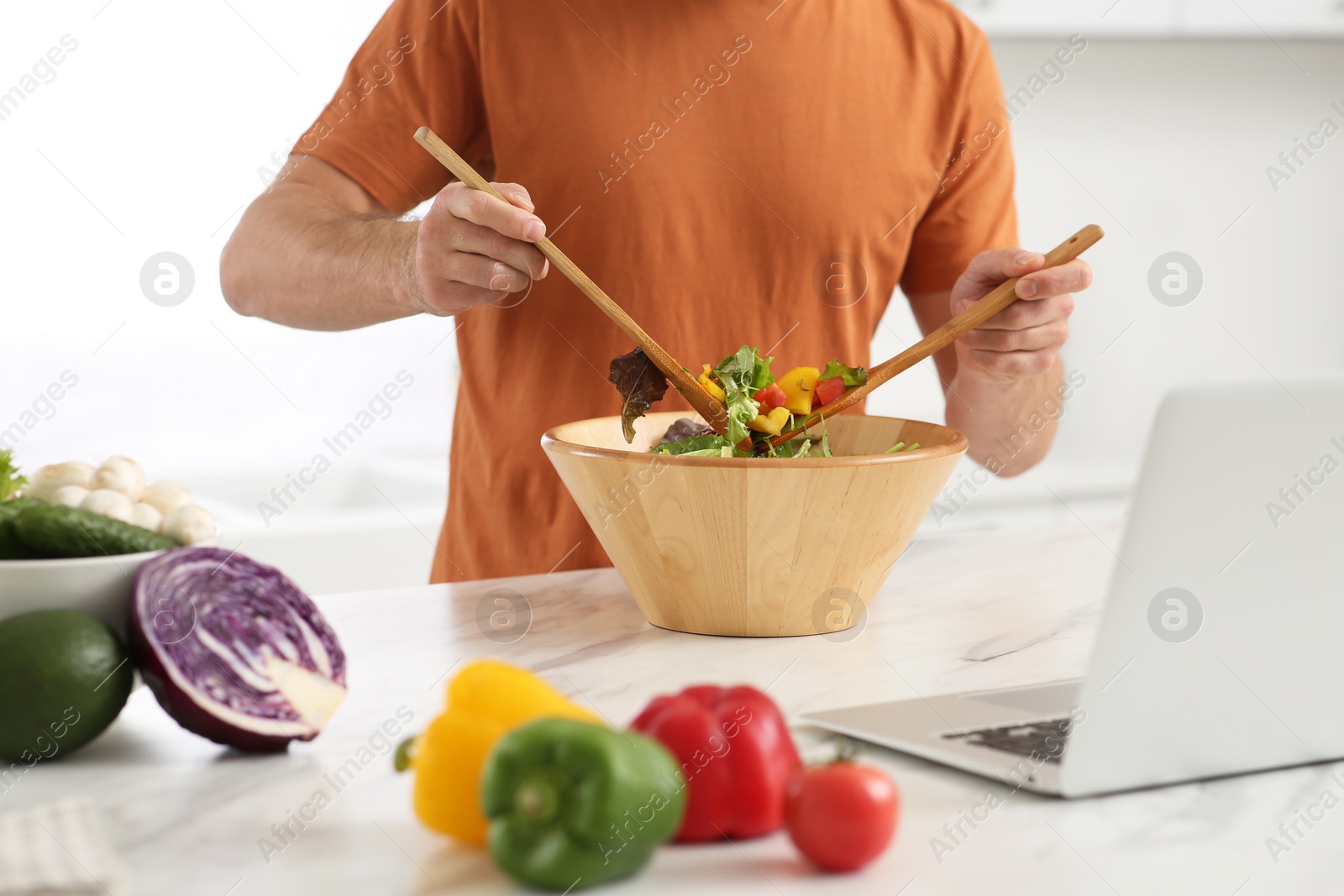 Photo of Man making dinner while watching online cooking course via laptop in kitchen, closeup