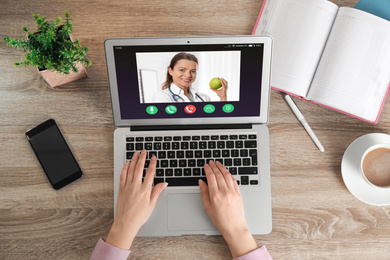 Woman using laptop for online consultation with nutritionist via video chat, top view