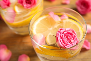 Tasty refreshing lemon drink with roses on wooden table, closeup