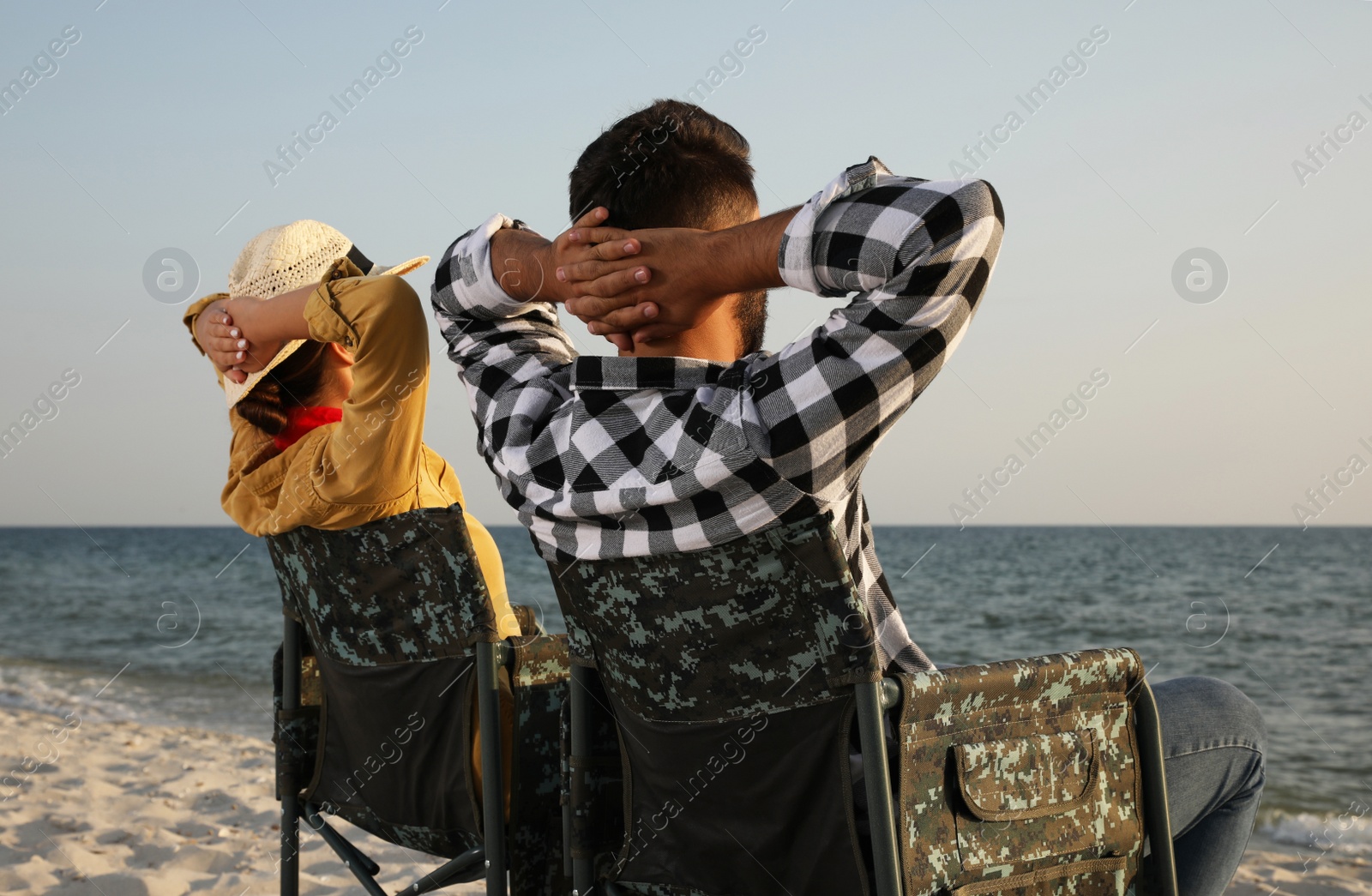 Photo of Couple sitting in camping chairs and enjoying seascape on beach