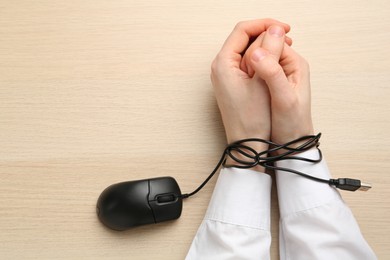 Photo of Man showing hands tied with computer mouse cable at wooden table, top view. Internet addiction