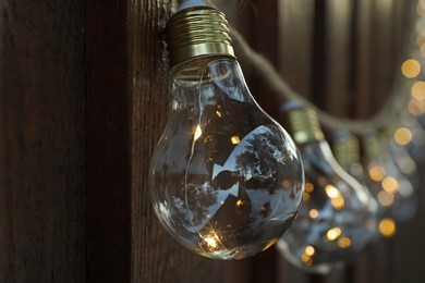 Photo of Garland of lamp bulbs hanging on wooden wall, closeup. String lights