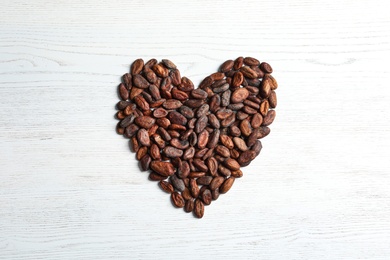 Heart made of cocoa beans on white wooden table, top view