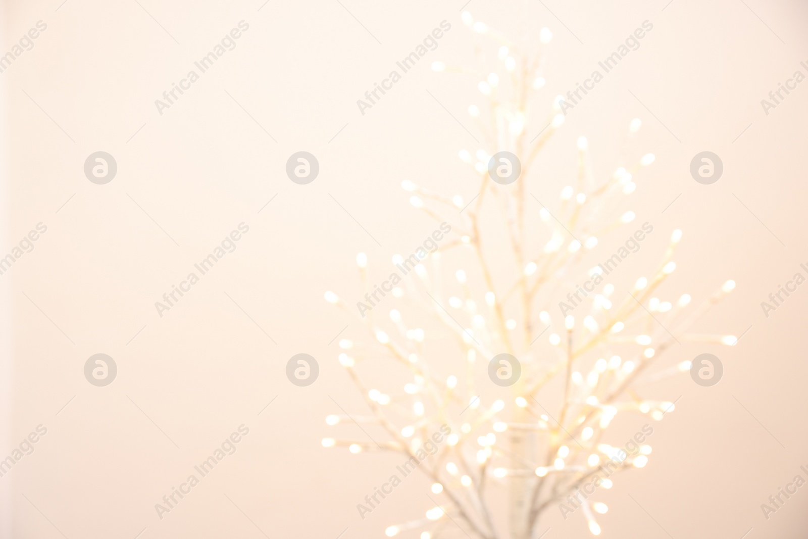 Photo of Decorative tree with lights on beige background, blurred view. Space for text