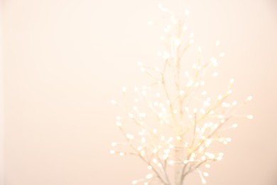 Decorative tree with lights on beige background, blurred view. Space for text