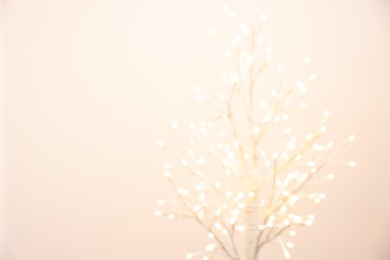 Photo of Decorative tree with lights on beige background, blurred view. Space for text