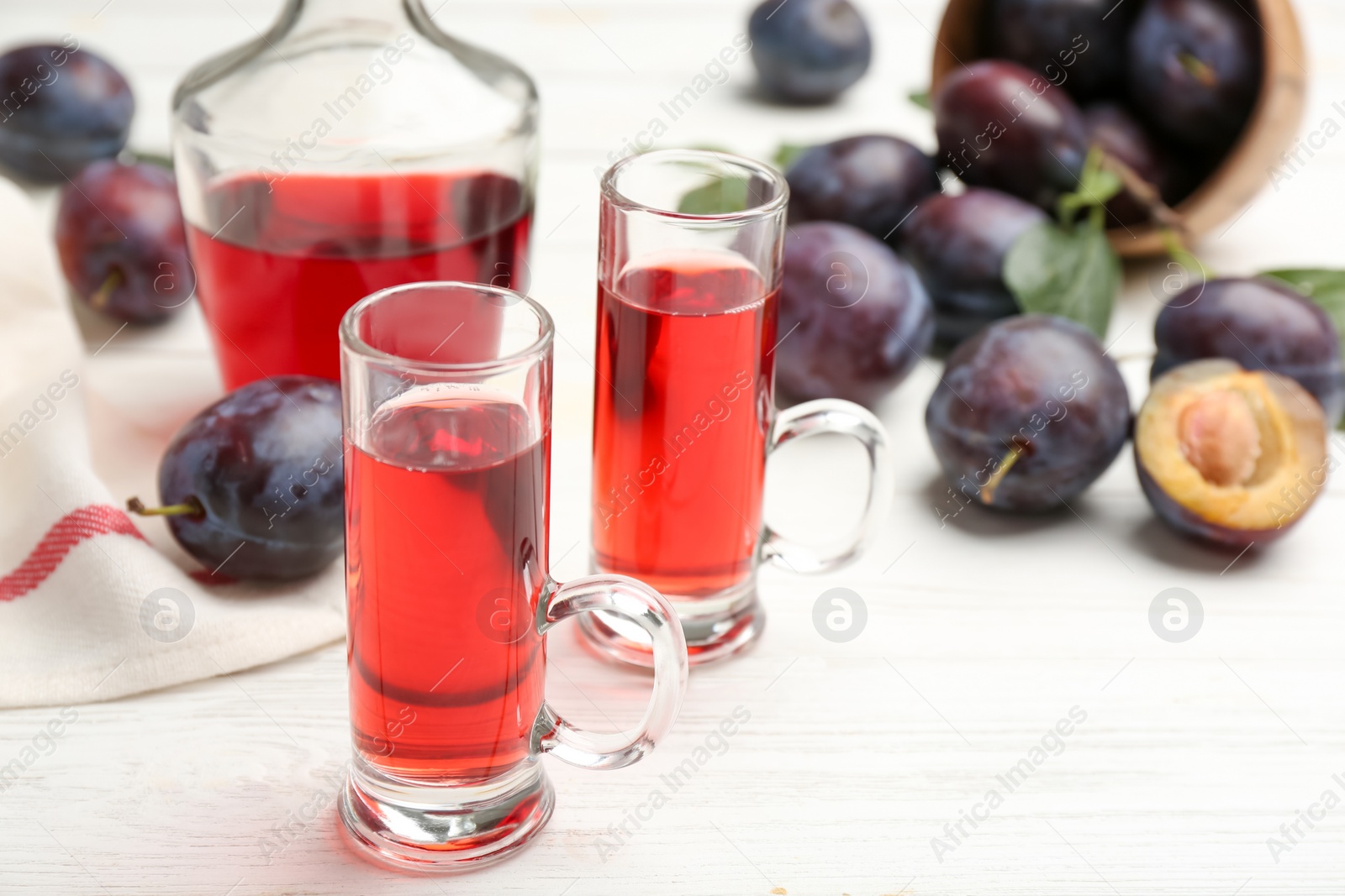 Photo of Delicious plum liquor and ripe fruits on white wooden table, closeup. Homemade strong alcoholic beverage