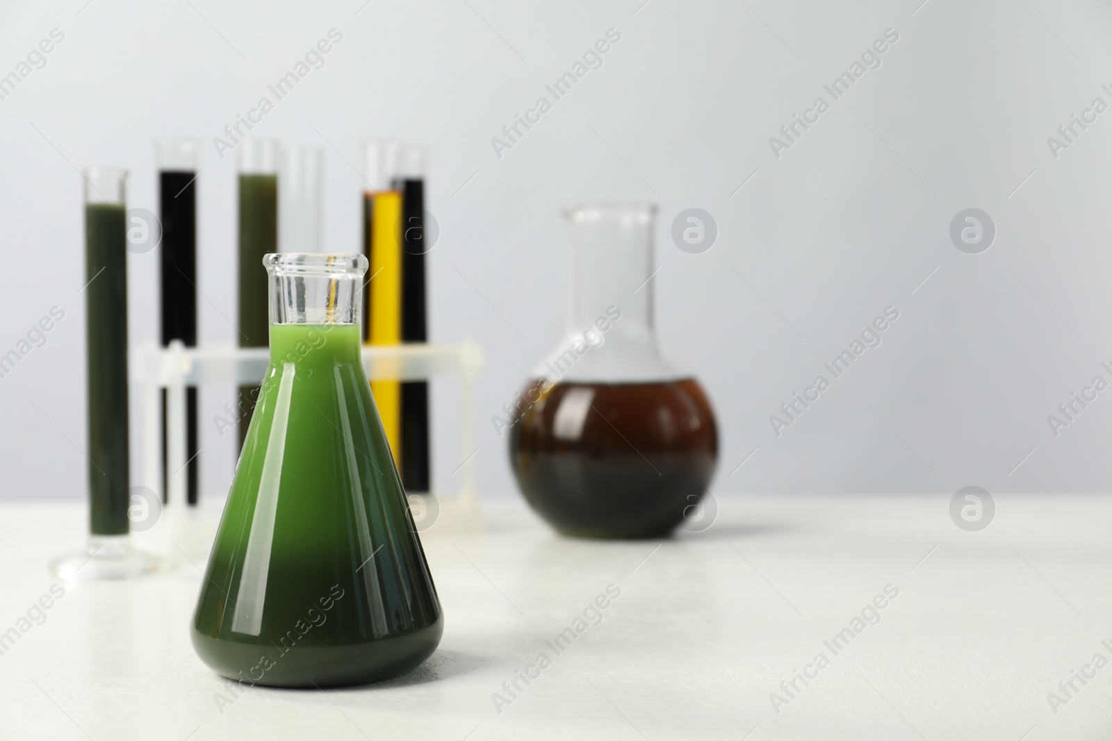 Photo of Laboratory glassware with different types of oil on white table, space for text