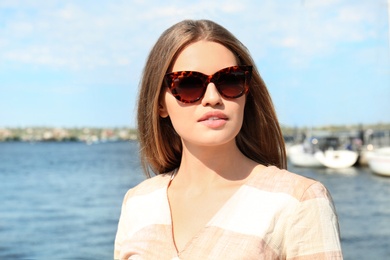 Photo of Young woman wearing stylish sunglasses near river