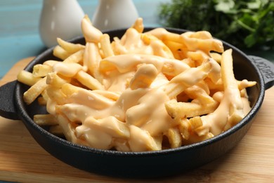 Delicious french fries with cheese sauce in bowl on wooden board, closeup