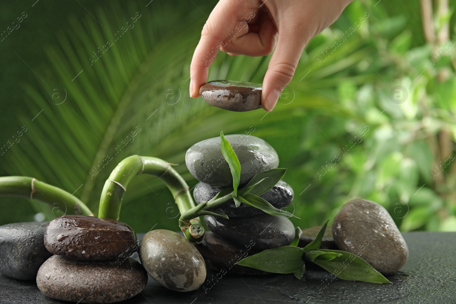 Photo of Woman stacking stones on table against blurred background, closeup. Zen concept