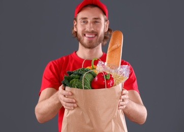 Photo of Delivery man holding paper bag with food products on dark background