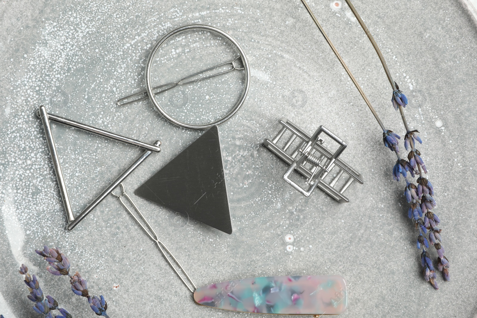 Photo of Stylish hair clips and flowers on grey table, flat lay