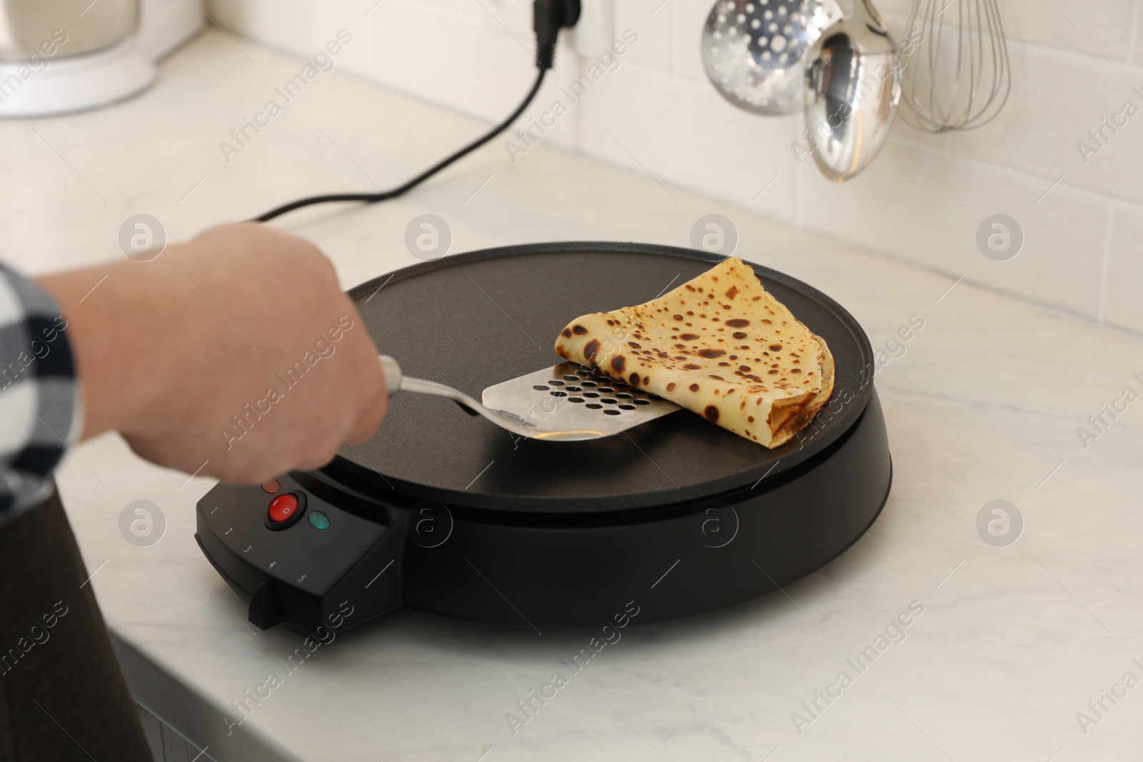 Photo of Man cooking delicious crepe on electric pancake maker in kitchen, closeup