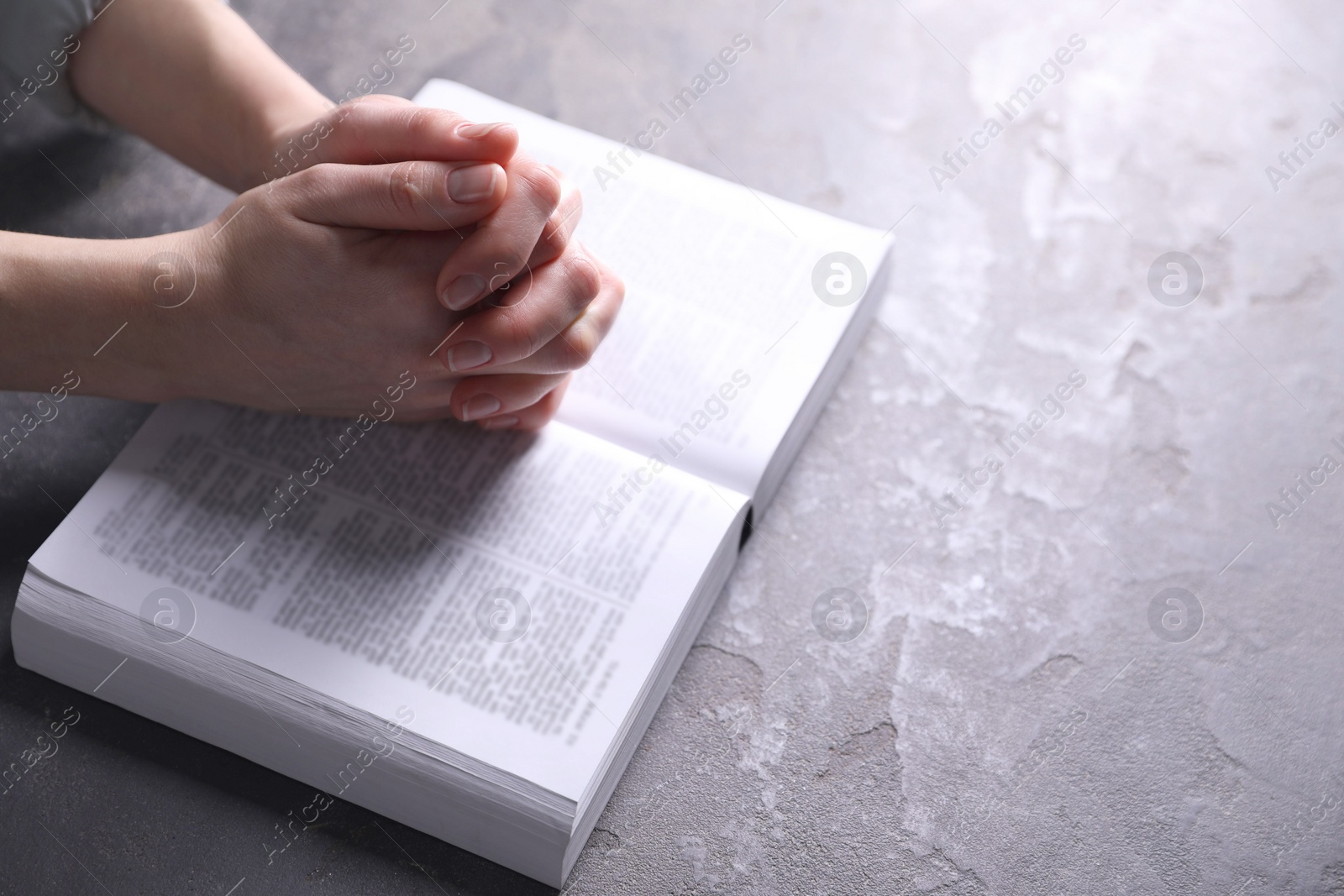 Photo of Religion. Christian woman praying over Bible at gray table, closeup. Space for text
