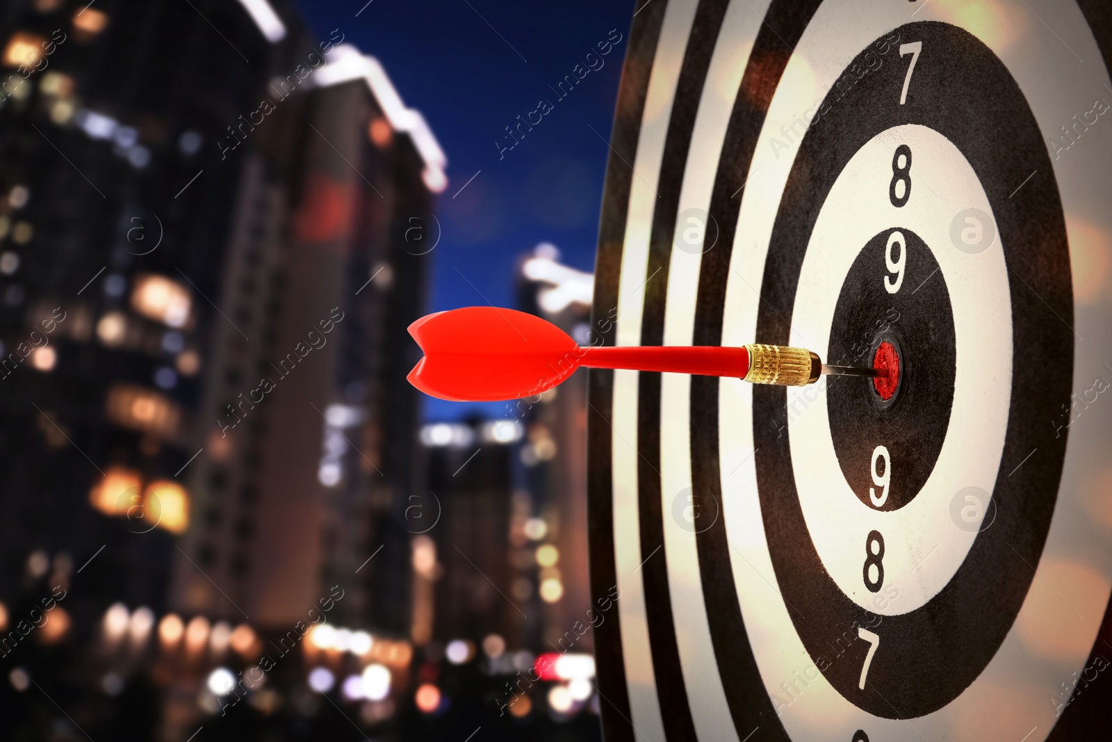 Image of Red dart hitting target on board against blurred of view night cityscape