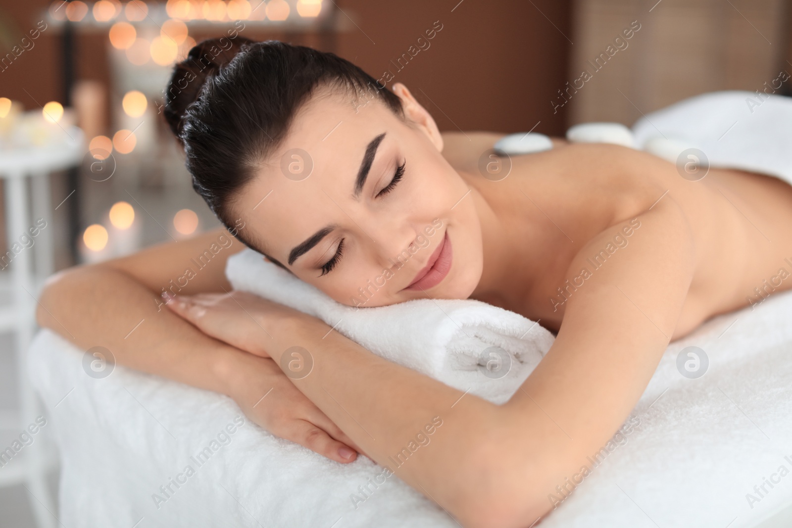 Photo of Young woman undergoing hot stone therapy in spa salon