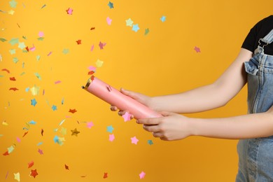 Photo of Young woman blowing up party popper on yellow background, closeup