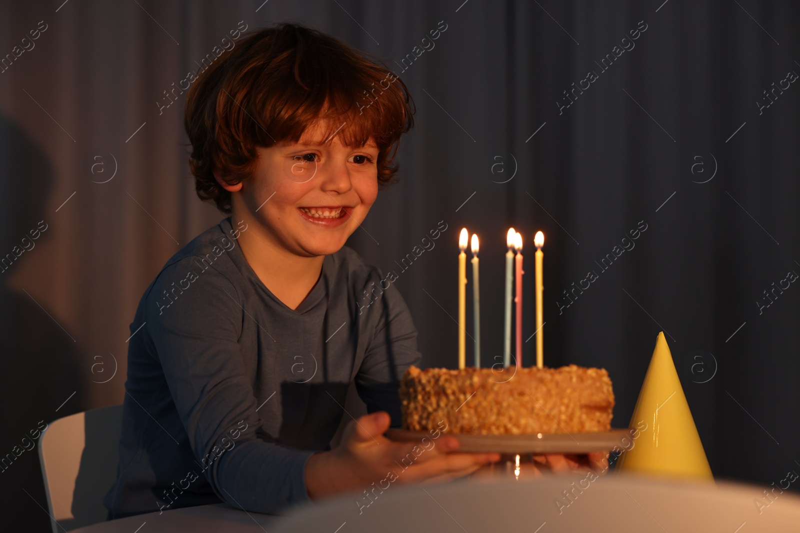 Photo of Cute boy with birthday cake at table indoors