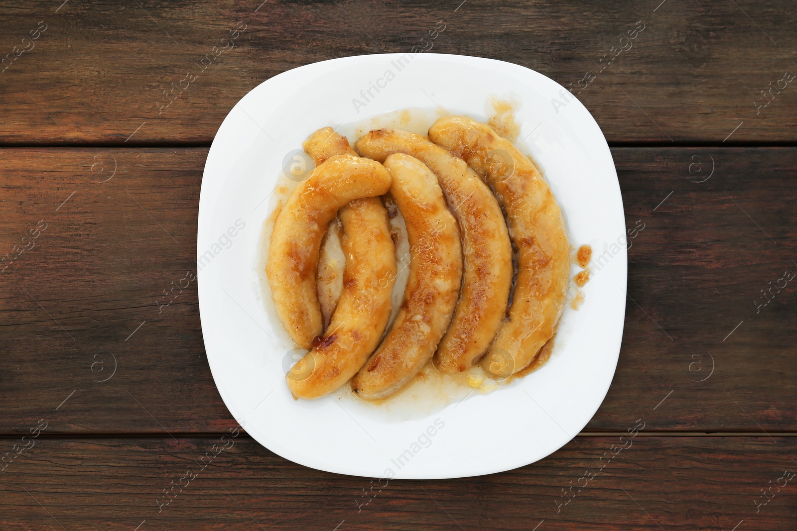 Photo of Plate with delicious fried bananas on wooden table, top view