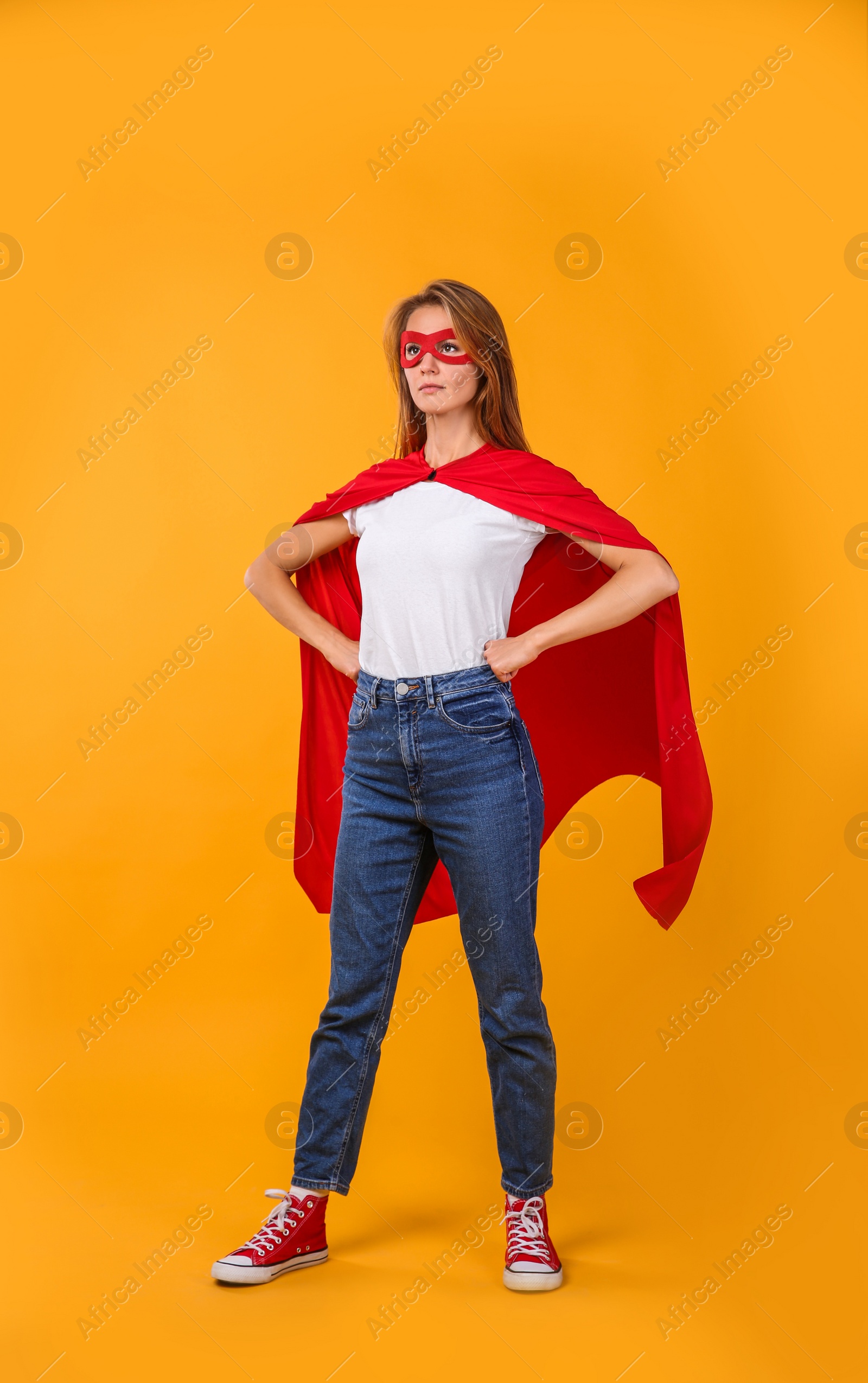 Photo of Confident woman wearing superhero cape and mask on yellow background
