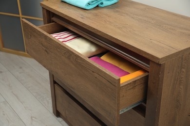 Photo of Wooden chest of drawers with different folded clothes indoors