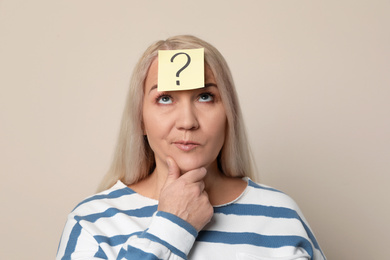 Photo of Emotional mature woman with question mark on beige background
