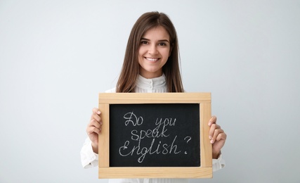 Photo of Young female teacher holding chalkboard with words DO YOU SPEAK ENGLISH? on light background