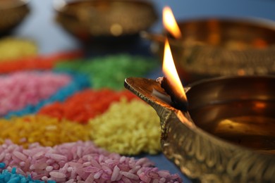 Diwali celebration. Diya lamps and colorful rangoli on blurred background, closeup. Space for text
