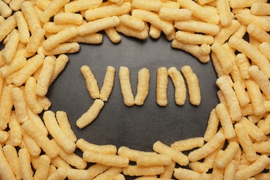 Photo of Word Yum made of corn sticks on dark grey table, flat lay