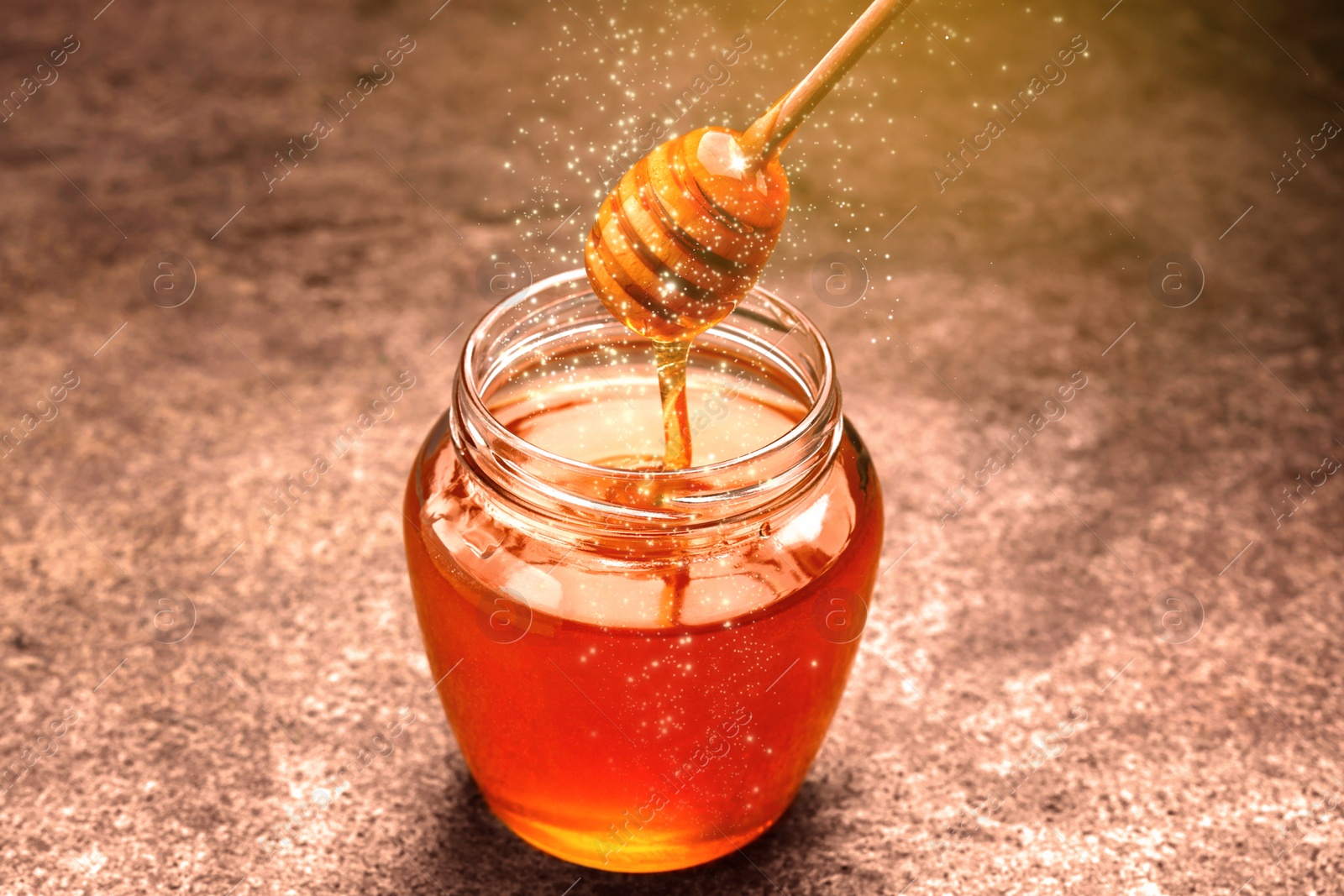 Image of Natural honey dripping from dipper into glass jar on table under sunlight