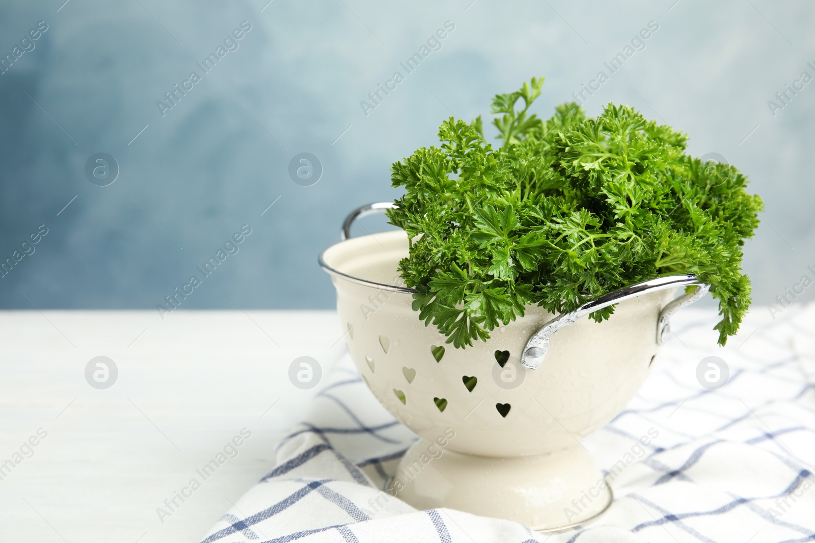 Photo of Colander with fresh green parsley on white table against color background. Space for text